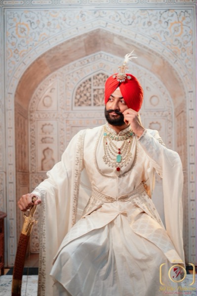 Sikh groom in a red turban with kalgi, cream sherwani and kirpan — Thind Turban Tying Centre UK