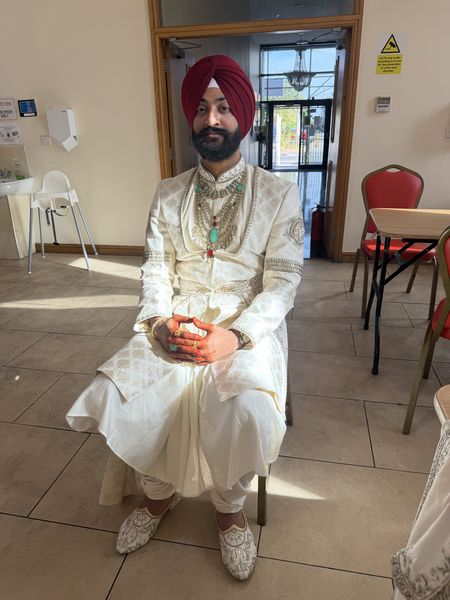 Sikh groom in a maroon turban and cream sherwani at his wedding venue